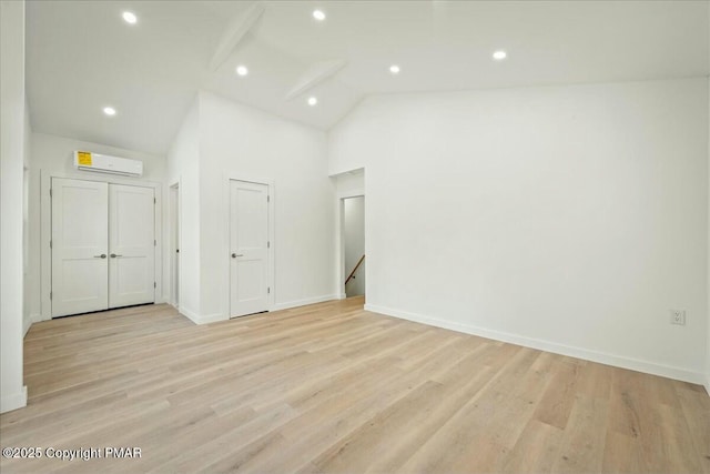 empty room with light hardwood / wood-style flooring, high vaulted ceiling, and a wall mounted AC