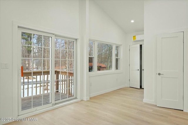 doorway to outside with light hardwood / wood-style flooring, high vaulted ceiling, and a wall mounted AC