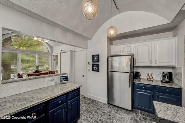 kitchen with white cabinetry, stainless steel fridge, vaulted ceiling, and blue cabinets