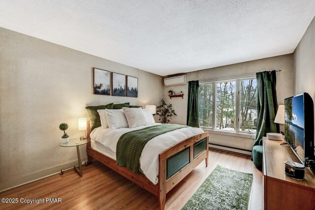 bedroom with a baseboard heating unit, a textured ceiling, a wall unit AC, and light wood-type flooring