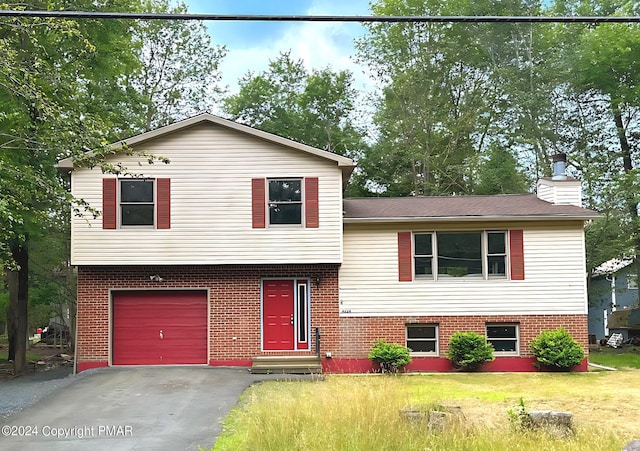 tri-level home with entry steps, driveway, a chimney, a front lawn, and brick siding