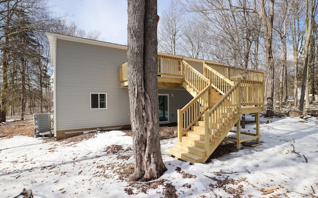 snow covered property with a wooden deck, stairway, and central AC unit