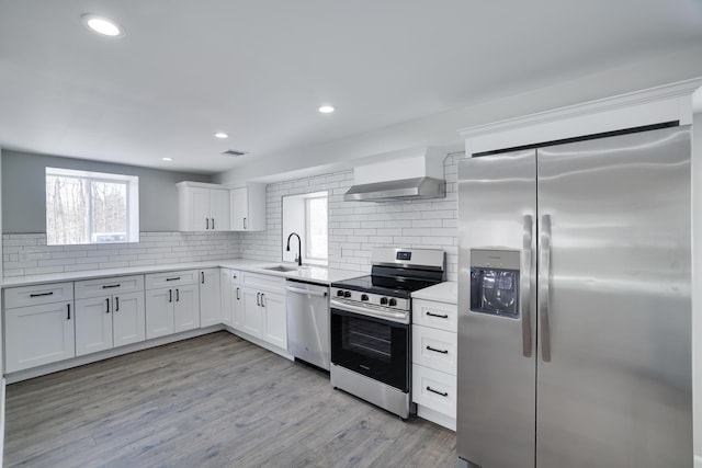 kitchen with tasteful backsplash, white cabinets, a sink, appliances with stainless steel finishes, and wall chimney exhaust hood