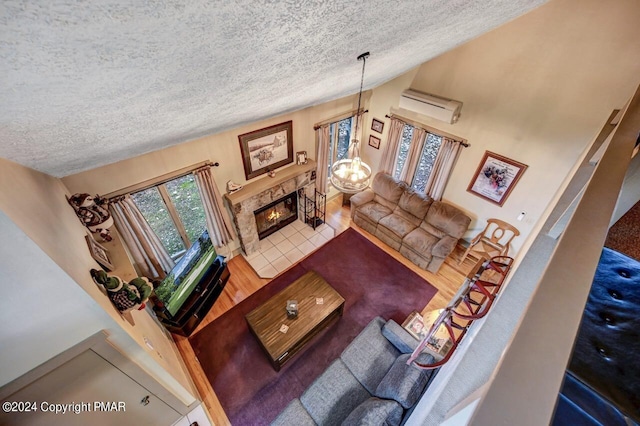 living area with a wall unit AC, a notable chandelier, a tiled fireplace, vaulted ceiling, and a textured ceiling