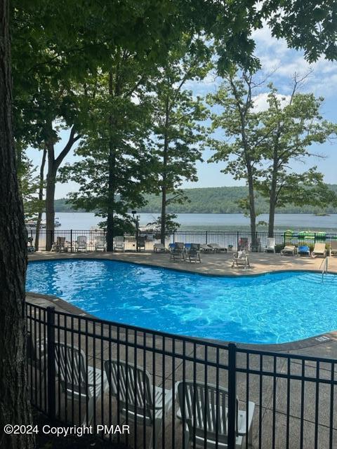 community pool with a patio, a water view, and fence