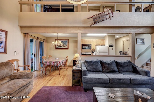 living room with a towering ceiling, an inviting chandelier, stairs, and wood finished floors