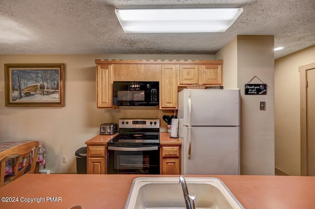 kitchen featuring black microwave, a sink, light countertops, freestanding refrigerator, and stainless steel electric range oven