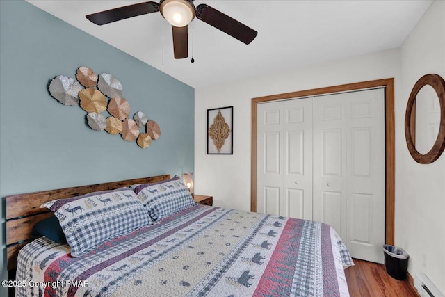 bedroom with a baseboard heating unit, a closet, wood finished floors, and a ceiling fan