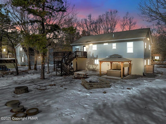 back of house with stairway, an outdoor fire pit, a deck, and a hot tub