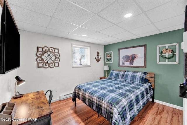 bedroom with a drop ceiling, baseboards, baseboard heating, and wood finished floors