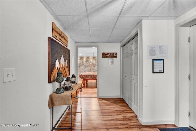 hall featuring a drop ceiling, light wood-style flooring, and baseboards