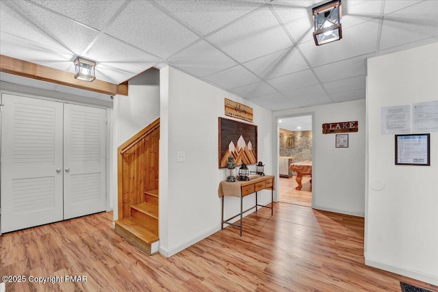 hallway featuring a drop ceiling, baseboards, light wood-style flooring, and stairs