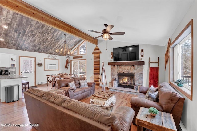 living area featuring light wood finished floors, a baseboard heating unit, lofted ceiling with beams, a stone fireplace, and ceiling fan with notable chandelier