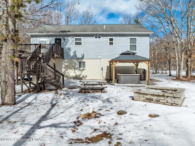 snow covered rear of property with a hot tub, stairs, a gazebo, a deck, and an attached garage