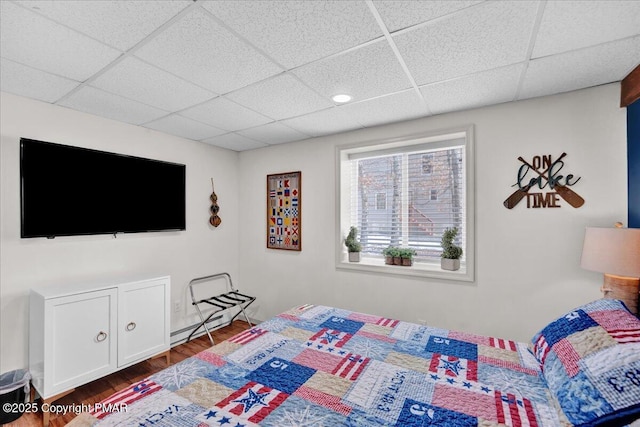 bedroom with a drop ceiling, a baseboard heating unit, and wood finished floors