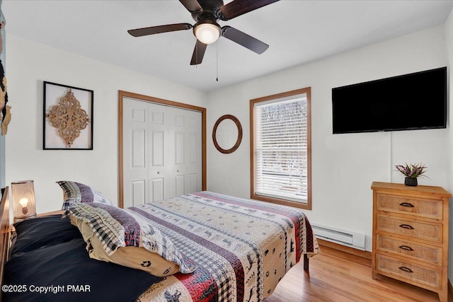 bedroom with a closet, light wood-style flooring, a ceiling fan, and a baseboard radiator