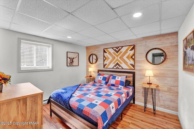 bedroom with a drop ceiling, baseboards, wood finished floors, and an accent wall