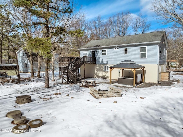 snow covered property featuring a fire pit, a hot tub, stairway, a wooden deck, and a gazebo