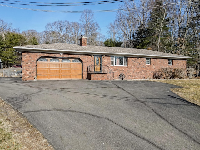 single story home featuring driveway, roof with shingles, a garage, brick siding, and a chimney