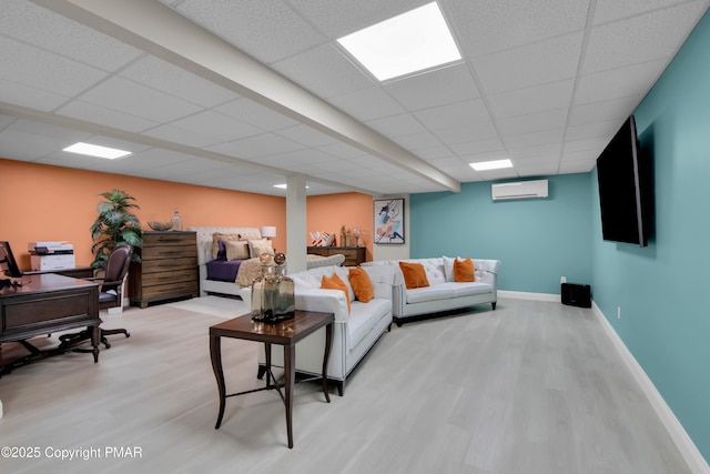 living area featuring light wood finished floors, a wall unit AC, a drop ceiling, and baseboards