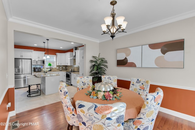 dining space with baseboards, visible vents, light wood-style flooring, ornamental molding, and a notable chandelier