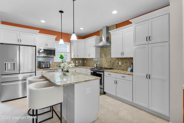 kitchen with stainless steel appliances, wall chimney range hood, white cabinetry, and a center island