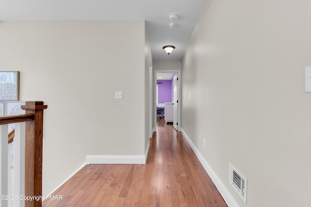 hallway featuring light wood-style flooring, visible vents, and baseboards