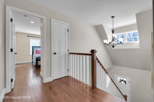 corridor with baseboards, wood-type flooring, an upstairs landing, a chandelier, and recessed lighting