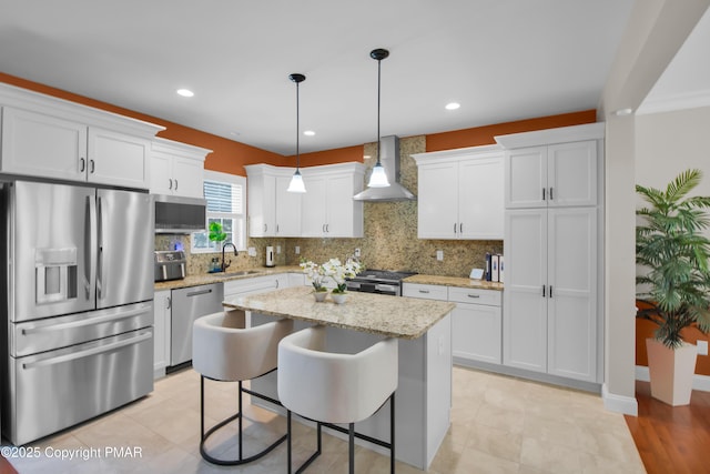 kitchen featuring a sink, a kitchen island, white cabinets, appliances with stainless steel finishes, and wall chimney range hood