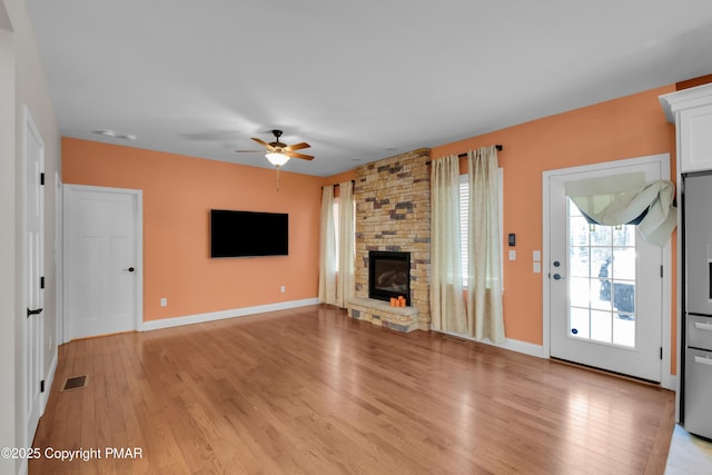 unfurnished living room featuring light wood-style floors, visible vents, a stone fireplace, and baseboards