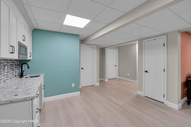 kitchen with tasteful backsplash, stainless steel microwave, white cabinets, a sink, and light wood-type flooring