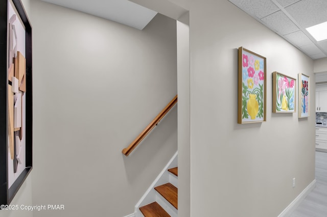 stairs featuring a paneled ceiling, baseboards, and wood finished floors