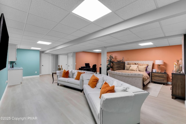 living room featuring baseboards, a drop ceiling, and light wood-style floors