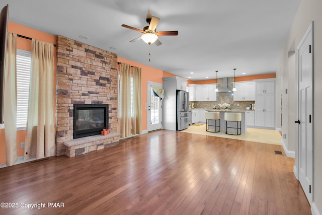 unfurnished living room with a stone fireplace, visible vents, ceiling fan, and light wood-style flooring