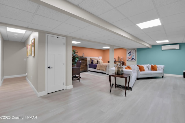 living room featuring light wood finished floors, a wall mounted AC, a paneled ceiling, and baseboards