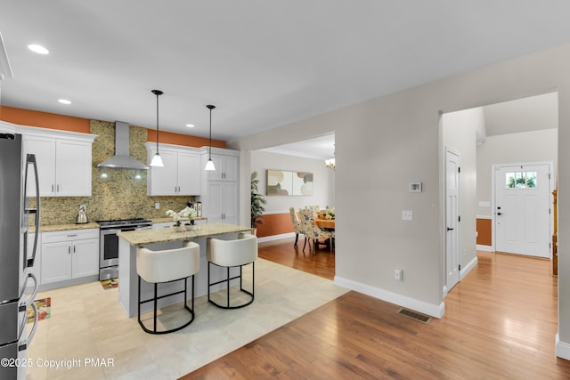 kitchen featuring visible vents, wall chimney exhaust hood, a breakfast bar area, stainless steel appliances, and backsplash