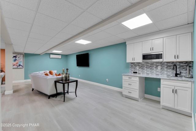 living area with light wood-type flooring, a paneled ceiling, and baseboards