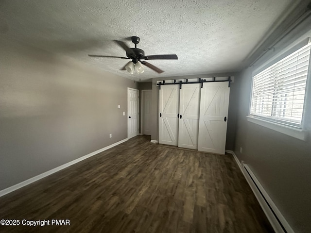 unfurnished bedroom with dark hardwood / wood-style floors, ceiling fan, baseboard heating, a barn door, and a textured ceiling