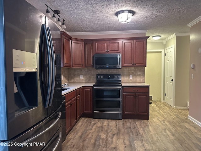 kitchen with appliances with stainless steel finishes, hardwood / wood-style floors, tasteful backsplash, ornamental molding, and a textured ceiling