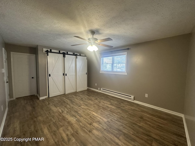 unfurnished bedroom featuring a baseboard heating unit, ceiling fan, a barn door, dark wood-type flooring, and a textured ceiling