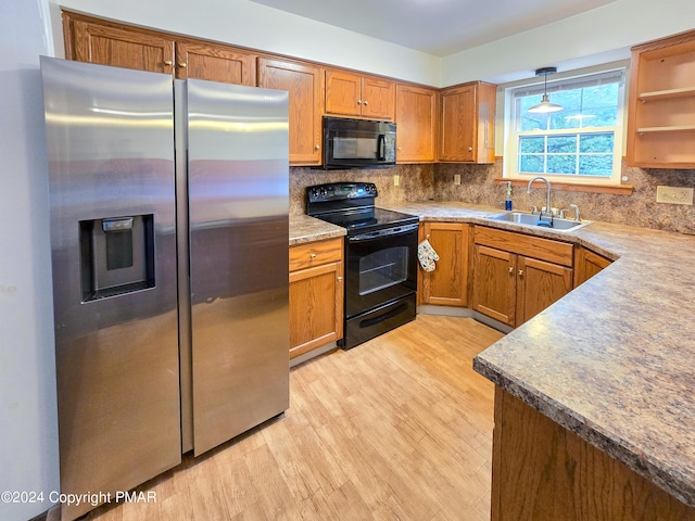 kitchen with light wood finished floors, decorative backsplash, brown cabinets, black appliances, and a sink