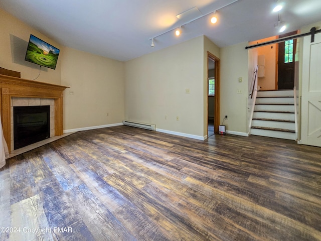 unfurnished living room with a barn door, baseboard heating, wood finished floors, and a tile fireplace