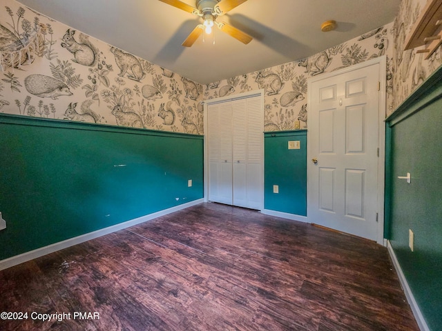 unfurnished bedroom with a closet, wainscoting, wood finished floors, baseboards, and wallpapered walls