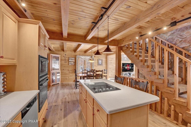 kitchen with wood walls, decorative light fixtures, light hardwood / wood-style flooring, a kitchen island, and black appliances