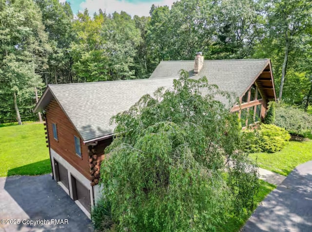 exterior space featuring a shingled roof, log siding, aphalt driveway, and a lawn