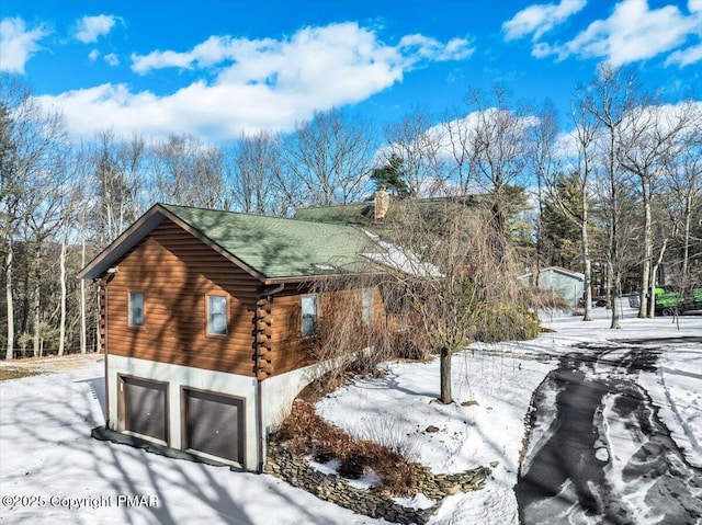 snow covered property featuring a garage, a chimney, and log siding