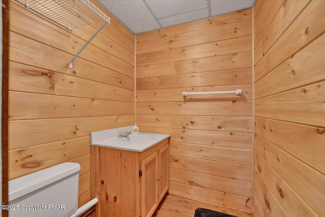 half bathroom featuring wooden walls, vanity, toilet, and wood finished floors