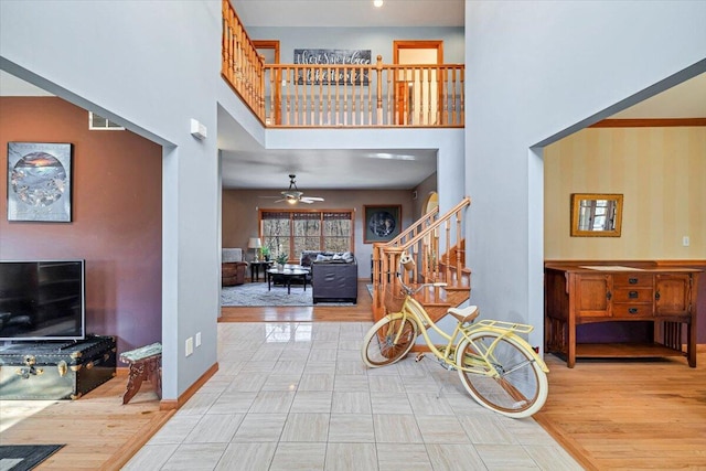 interior space featuring baseboards, visible vents, ceiling fan, stairs, and a towering ceiling