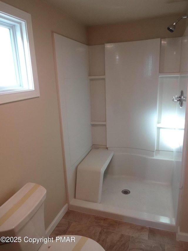 bathroom featuring toilet, baseboards, and a shower