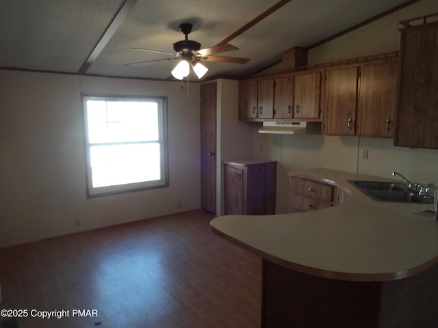 kitchen featuring lofted ceiling, light countertops, brown cabinetry, a sink, and a peninsula